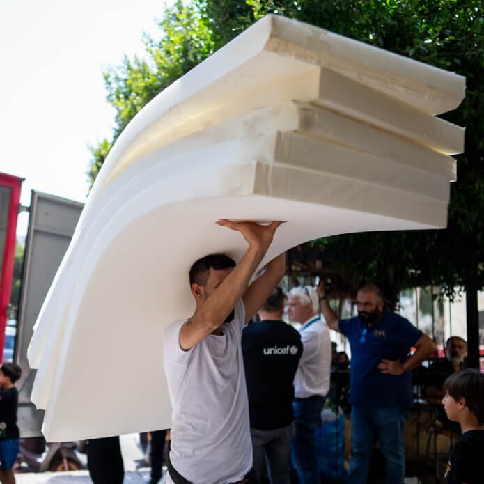 hombre cargando colchones nuevos en un campamento de refugiados de UNICEF