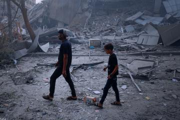 Fotografía de un niño y su padre caminando entre los escombros de su hogar, destruido en Gaza