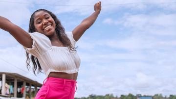 joven mujer abriendo los brazos feliz mirando al camara con un lindo cielo de fondo