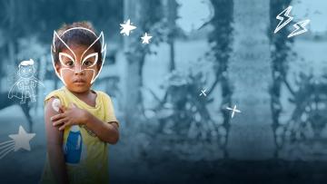 nino con mascara de super heroe pintada sobre la fotografia mostrando su brazo orgulloso de haber sido vacunado
